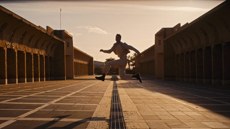 Still cinematográfico del fashion film “Architecture of Tailoring” SS26. Composición simétrica con luz natural controlada y arquitectura de madera enmarcando al modelo.